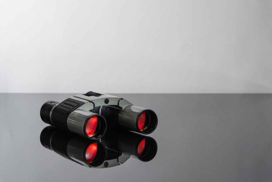 Close-up of modern binoculars with red lenses reflecting on a sleek glass surface.