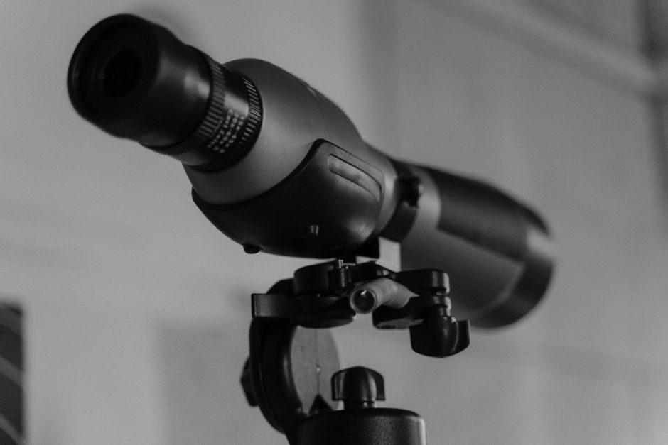 Detailed monochrome image of a modern telescope lens mounted on a tripod.