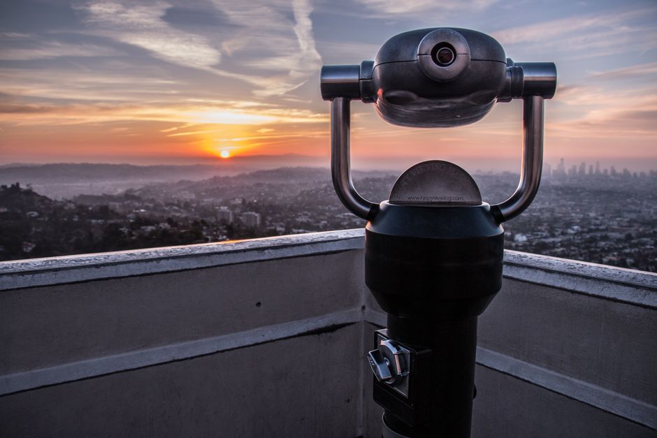 A coin operated telescope on a rooftop, overlooking a stunning cityscape at sunset.